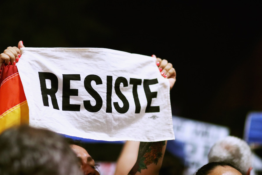 A protester in Downtown Phoenix holds up a white flag with black text that says Resiste. Protesters congregated outside the building where President Donald J. Trump held a campaign-style rally on Tuesday, Aug. 22, 2017.