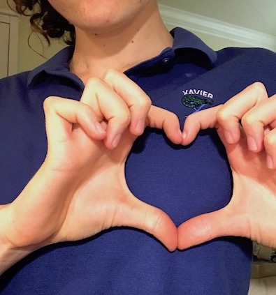 A Xavier student makes a heart symbol over her Xavier uniform, showing how Xavier students care for the world around them. 