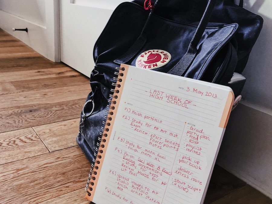 A planner with a list of tasks written down leans against a grey backpack.