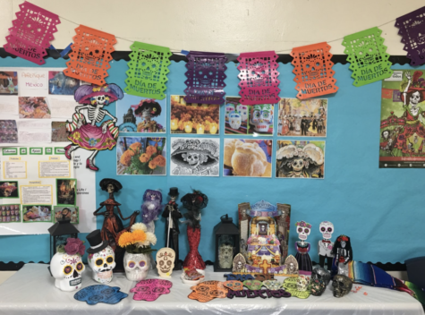 Sra. Gutiérrez’s ofrenda is decorated with calaveras, papel picado, photos of other traditional items, and physical depictions of La Calavera Catrina and El Catrín.