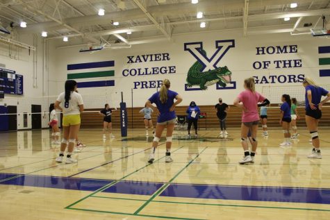 Xavier’s varsity volleyball players along with the coaches start off their practice in a socially-distanced group circle.