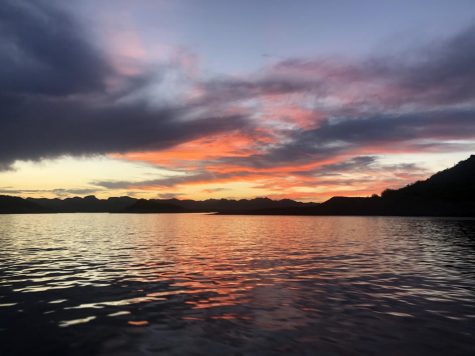 A summer sun sets behind a mountain on Lake Pleasant and reflects on the lake’s water.