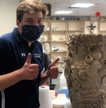 Zachary Carlson, ceramics teacher, stands with a ceramics project. Carlson has been working on providing a creative, yet safe space for students to work. 