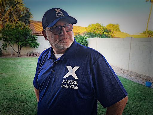 Luigi Cusano tries on his new Xavier Dads’ Club merchandise gifted to him after his first club meeting. Included in the lifetime membership are a ski-trip discount, free access to all XCP and BCP home games, Dads’ Club polo shirt, event discounts, name tag and baseball cap. (Photo courtesy of Mariella Cusano, Club Photographer)