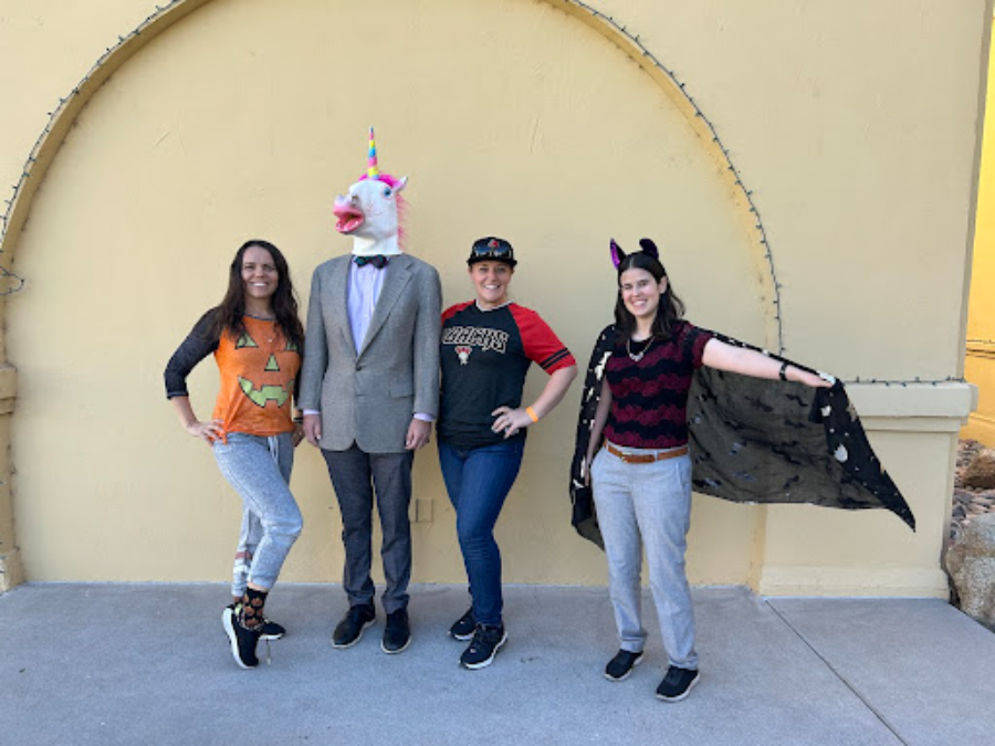 Xavier teachers line up in front of the bell tower to show off their Halloween costumes and outfits. Eva Becker shows off her matching pumpkin shirt and socks, Dr. Clay Zuba stands proudly in his “Fran” headpiece, Peggy Sue Clay shows her Diamondbacks pride and Sarah Schimpp strikes a pose as a friendly bat.  (Photo courtesy of Chloe Beery)