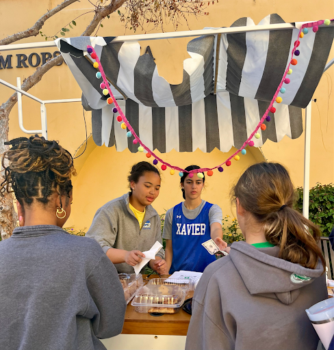 Zoie Alexander ‘26, pictured left, sells brownies, muffins and other baked goods at the Christmas Market on December 6, 2023. She sold these items from a festive cart in the center of Xavier College Preparatory’s campus.  (Photo courtesy of Ellie Hilsabeck, XPress Staff)