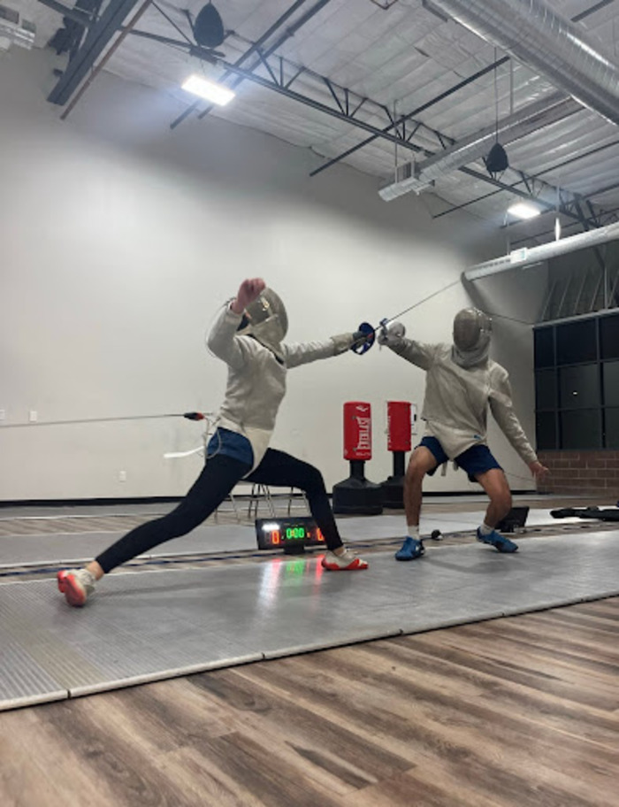 Eva+Wilson+lunges+toward+her+opponent+at+a+lesson+on+Friday%2C+April+12+at+Phoenix+Fencing+Academy.+Both+fencers+are+wearing+the+metal+jackets+that+are+connected+to+strips+with+cords+that+detect+when+they+are+hit.