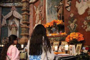 Sophia Reyes ‘26 and Camilla Gonzales ‘26 observe a Día de los Muertos altar decorated with candles, marigolds and traditional offerings. The display was created to honor loved ones and teach students about the cultural significance of the holiday.